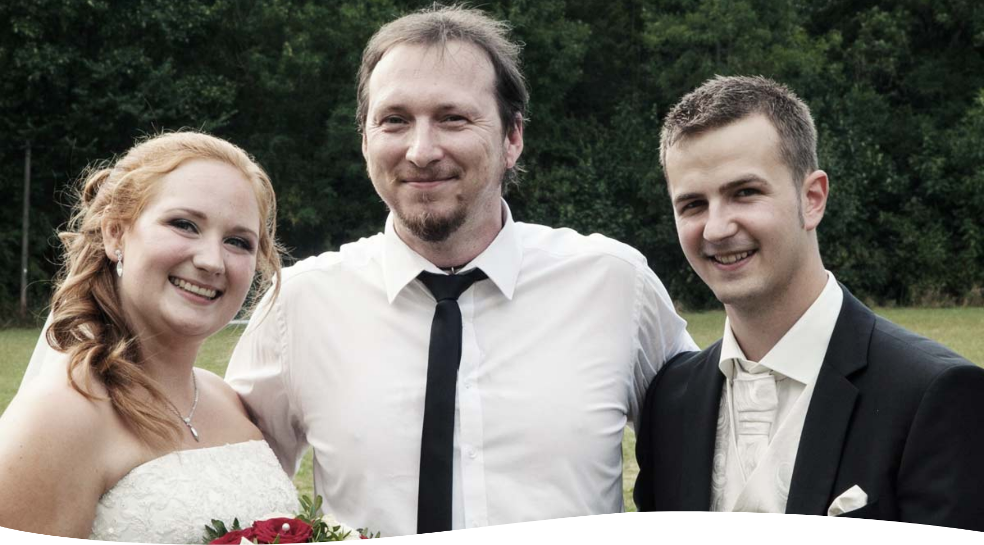Ein Brautpaar posiert mit ihrem Hochzeits-DJ Landshut für ein Foto auf einem Feld.