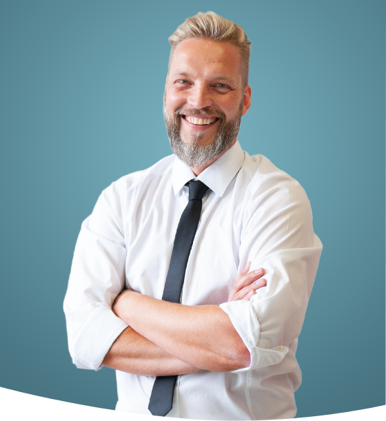 Ein selbstbewusster Mann mit Bart, der lächelt, während er mit verschränkten Armen steht, gekleidet in ein weißes Hemd und eine Krawatte vor einem blaugrünen Hintergrund.