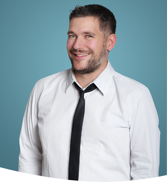 Mann in weißem Hemd und Krawatte lächelt vor einem blaugrünen Hintergrund.