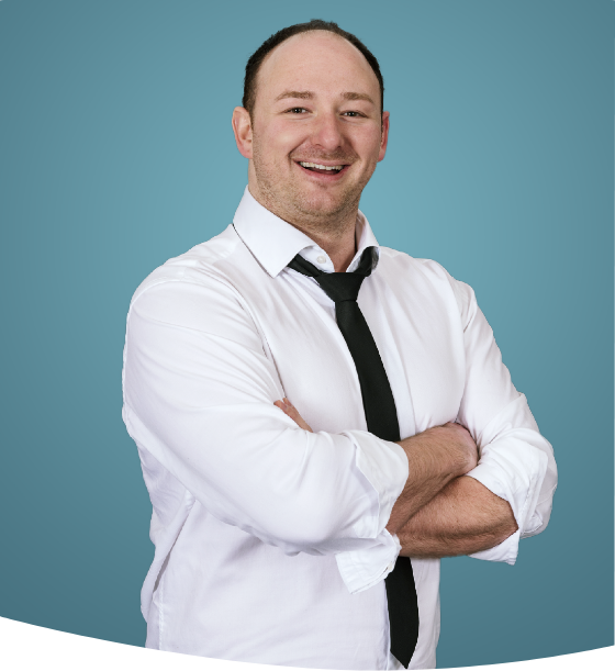Ein lächelnder Mann in einem weißen Hemd mit hochgekrempelten Ärmeln und schwarzer Krawatte steht mit verschränkten Armen da.