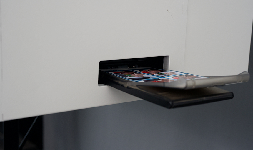 Fotodrucke, die teilweise aus dem Schlitz einer Fotokabine kommen, auf einem Smartphone in einer durchsichtigen Hülle. Fotodrucke, die teilweise aus dem Schlitz einer Fotokabine kommen, auf einem Smartphone in einer durchsichtigen Hülle.