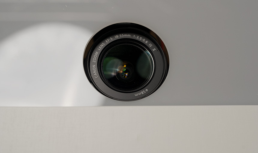 Nahaufnahme eines Canon-Zoomobjektivs mit den Spezifikationen 18–55 mm und 1:3,5–5,6 vor einer reflektierenden Oberfläche. Nahaufnahme eines Canon-Zoomobjektivs mit den Spezifikationen 18–55 mm und 1:3,5–5,6 vor einer reflektierenden Oberfläche.