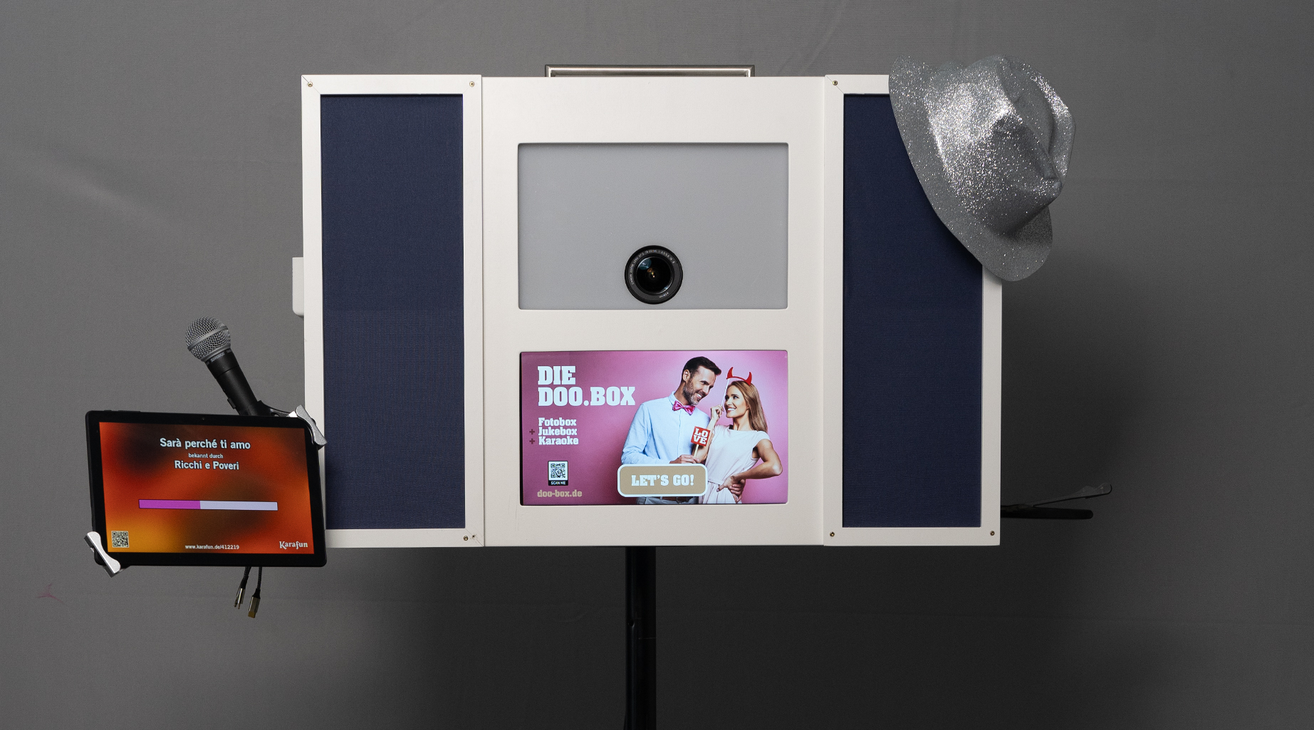 Digitale Fotokabine mit Kamera, Touchscreen, Mikrofon und einem silbernen Hut an der Seite.